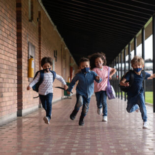 Group of Latin American children running at the school looking very excited to be back and wearing facemasks during the COVID-19 pandemic
